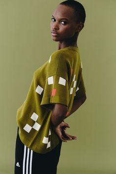 a woman in a green shirt and black pants poses for the camera with her hands on her hips