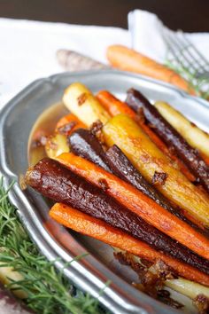 cooked carrots and other vegetables on a silver plate with rosemary sprigs in the background