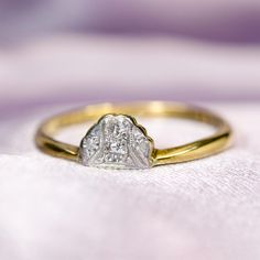 a gold and white diamond ring sitting on top of a cloth covered tablecloth in front of a light purple background