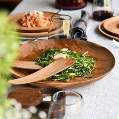 a wooden bowl filled with greens on top of a table next to other plates and glasses