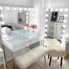 a white vanity with stool, mirror and lights in the room that is decorated with flowers