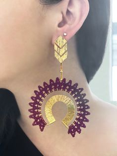 a close up of a woman's ear wearing gold and red earrings with an intricate design