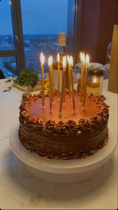 a birthday cake with lit candles sitting on a table in front of a large window