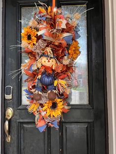 a fall wreath with sunflowers, leaves and a scarecrow on the front door