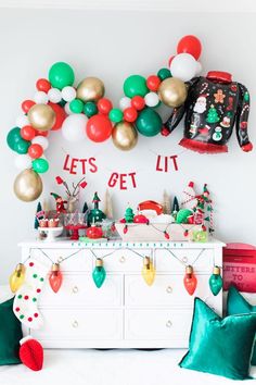 a christmas themed party with balloons, garlands and presents on a dresser in front of a white wall