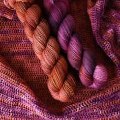 three skeins of yarn are laying on top of each other in shades of purple and orange