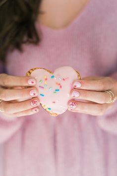 a woman holding a heart shaped doughnut with sprinkles in her hands