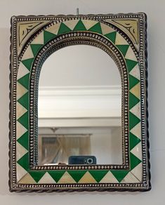 a mirror hanging on the wall with a green and white design in front of it