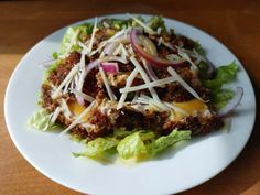 a white plate topped with lettuce and meat covered in cheese on top of a wooden table