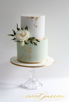 a three tiered cake with white and gold flowers on the top is sitting on a pedestal