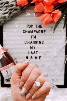 a woman is holding her wedding ring in front of a sign that says pop the champagne i'm changing my last name