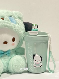 a green teddy bear sitting next to a cup with a strap around it's neck