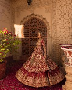 a woman in a red and gold bridal gown standing next to a potted plant