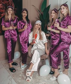 a group of women dressed in purple pajamas and holding wine glasses pose for the camera