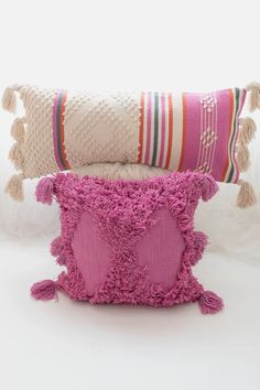 two pillows with tassels are stacked on top of each other