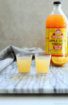 two glasses filled with liquid sitting on top of a marble table next to an orange bottle