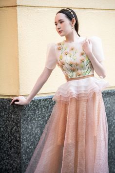 a woman in a pink dress standing next to a wall with her hands on her hips