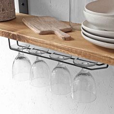 wine glasses are lined up on a shelf next to plates and utensil holders