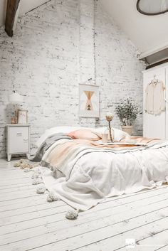 a bedroom with white brick walls and wooden flooring is decorated in pastel tones