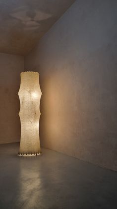 a tall white vase sitting in the middle of a room next to a light fixture