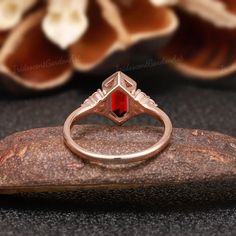 a gold ring with a red stone in the center on top of a rock next to flowers