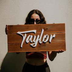 a woman holding up a wooden sign that says taylor