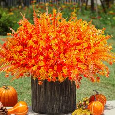 an arrangement of orange and yellow flowers in a wooden vase on a table with pumpkins