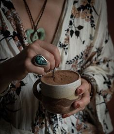 a woman is holding a cup with something in it and has a ring on her finger