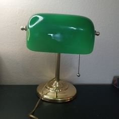 a green table lamp sitting on top of a black desk next to a white wall