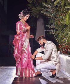 a man kneeling down next to a woman in a pink sari and white dress