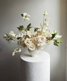 there is a white vase with flowers in it on top of a cake stand next to a window