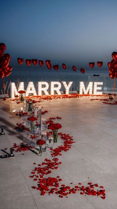 a large sign that says marry me surrounded by rose petals on the ground and balloons in the air