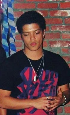 a young man standing in front of a brick wall with his eyes closed and hands clasped