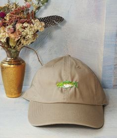 Introducing the Salmon Hat: hand-embroidered to honor the vital role of salmon in our ecosystems. This hat is a unique tribute to this keystone species, ensuring you stand out with environmental consciousness. Made with love from 100% cotton, featuring an adjustable back for a perfect fit. Khaki Fishing Cap, Khaki Cap For Fishing, Fish Hat, Keystone Species, Environmental Consciousness, Embroidered Hat, Embroidered Hats, Dad Hat, Adjustable Hat