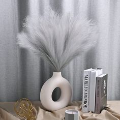 a white vase sitting on top of a table next to two books and a plant