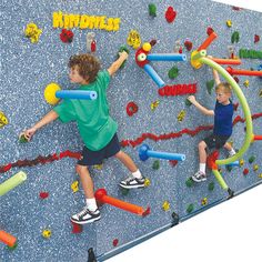 two young boys are climbing on a wall with plastic tubes and balls in the gym