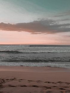 a person walking on the beach at sunset with their surfboard in hand and footprints in the sand