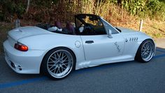 a white sports car is parked on the side of the road in front of some bushes