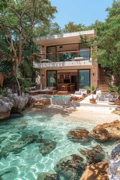 the house is surrounded by trees and rocks, with clear water in front of it