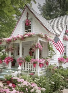 a white house with pink flowers and an american flag hanging from the front porch window