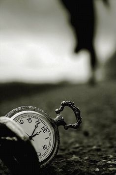 an old pocket watch sitting on the ground with a person walking by in the background