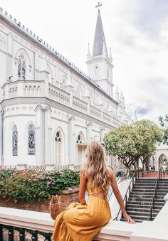 a woman in a yellow dress is sitting on some steps looking out at the building