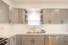 an empty kitchen with stainless steel appliances and white counter tops, along with gray cabinets