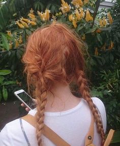 a girl with red hair is looking at her cell phone and has braids in her hair