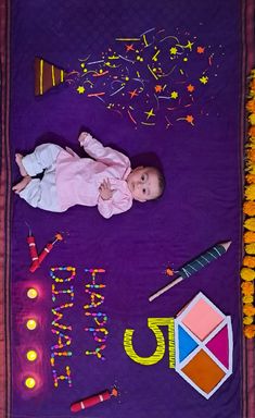 a baby laying on top of a purple blanket next to some candles and confetti