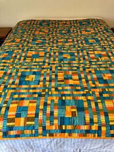 the bed is made up with an orange, blue and yellow quilt on top of it