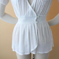 A stunning 1930s vintage blouse. Crisp, white cotton gauze with floral appliqué embroidery. Lap over short sleeves with plunging v-neck, elastic smocked waistband with double button and wrap front bust. All trim is lined with petite lace. Measurements of garment, allow space for fit.Taken flat, doubled for circumferenceShown on a size 4 dress formBust: 40”Waist: 22-28”Hips: 40”Shoulder: 16”Length: 24”Sleeve: 5.5”Tag: noneFabric: gauzy cottonCondition: Very good vintage. Buttons have been replace Fitted Smock V-neck Top, Fitted V-neck Coquette Tops, Vintage Summer Tops With Smocked Bodice, Vintage Smocked Bodice Top For Summer, V-neck Blouse With Smocked Bodice For Daywear, Fitted Peasant Blouse With V-neck, Fitted Smock V-neck Blouse, Fitted V-neck Peasant Blouse, Fitted V-neck Smock Blouse