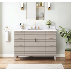 a bathroom vanity with two sinks and a mirror above it, next to a potted plant