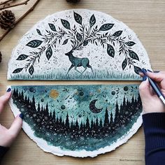 a person is drawing on a paper plate with trees and stars in the background, while another hand holds a pen