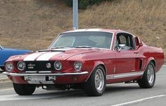 a red and white mustang driving down the road